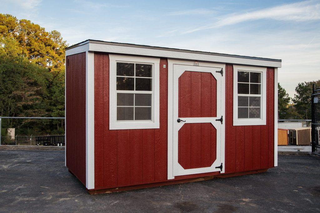A red shed with white trim and windows is sitting in a parking lot.