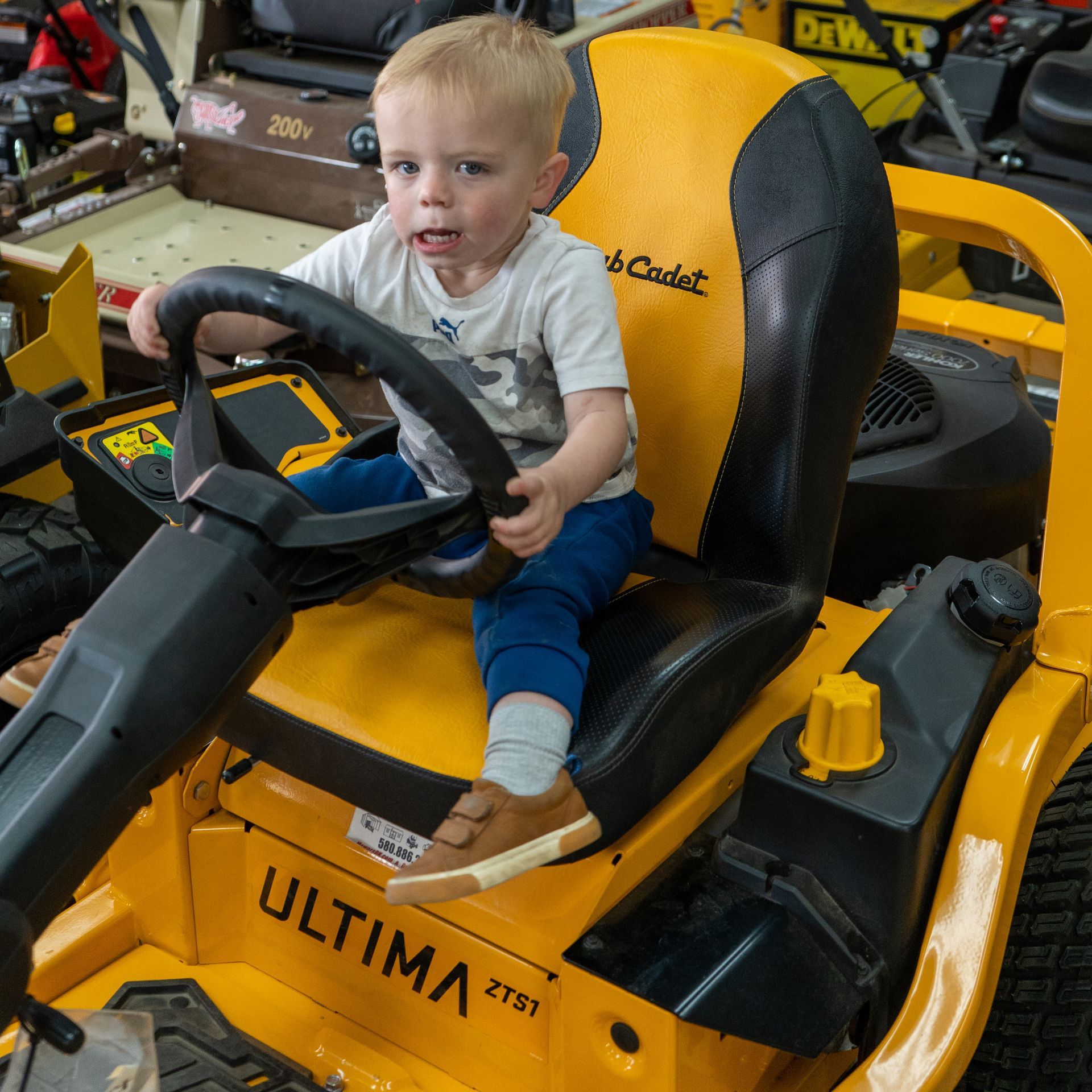 A little boy is sitting on a yellow ultima lawn mower