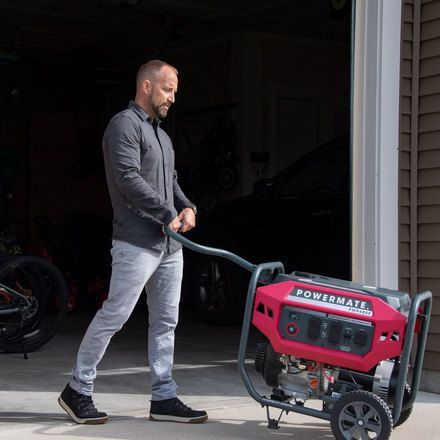 A man is pushing a red generator in a garage.