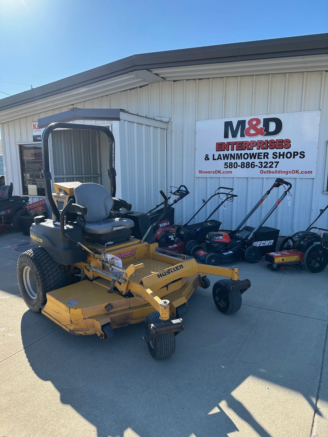 A yellow lawn mower is parked in front of M&D Enterprises Canton Oklahoma.