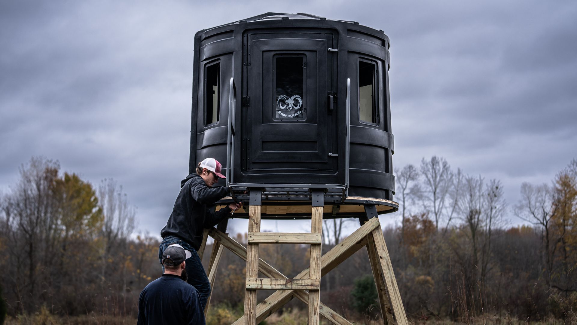 Two men are working on a deer stand in a field.