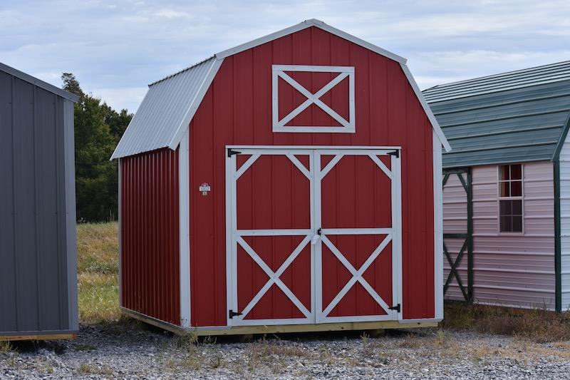 A red barn with white trim is sitting in the middle of a gravel field.