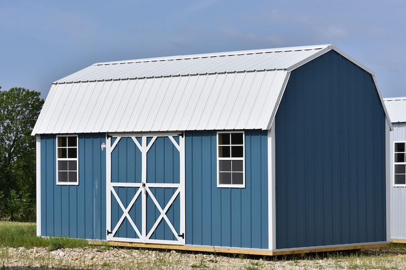 A blue barn with a white roof is sitting in the middle of a field.