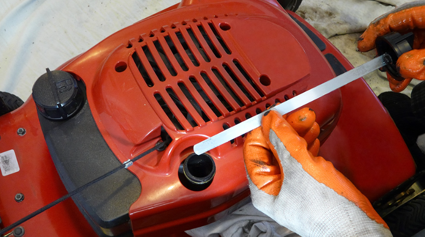 A person wearing orange gloves is working on a red lawn mower.