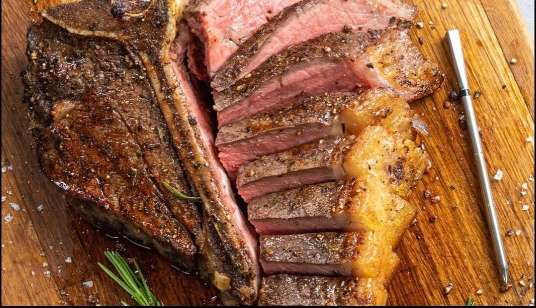 A large piece of steak is sitting on top of a wooden cutting board.