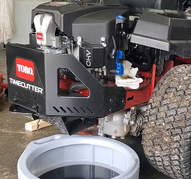 A toro timecutter lawn mower is sitting in a garage next to a bucket of oil.