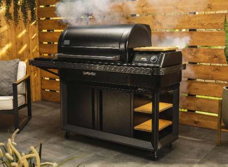 A black grill with smoke coming out of it is sitting on a patio next to a chair.