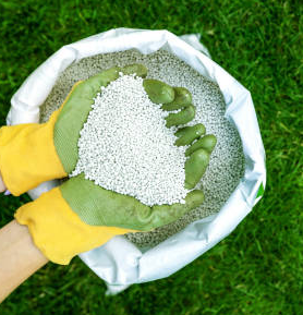 A person wearing yellow gloves is holding a bag of fertilizer in their hands.