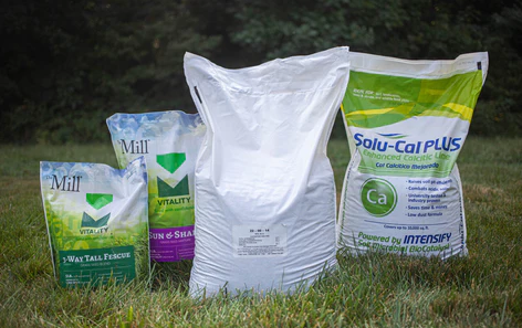 Three bags of fertilizer are sitting on top of a lush green field.