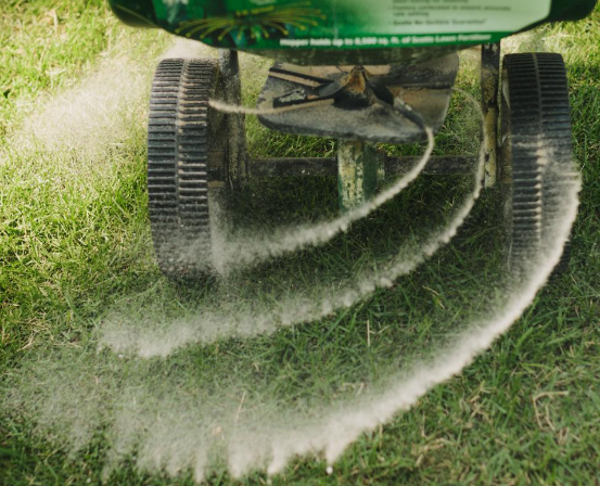 A person is spreading fertilizer on a lawn with a spreader.