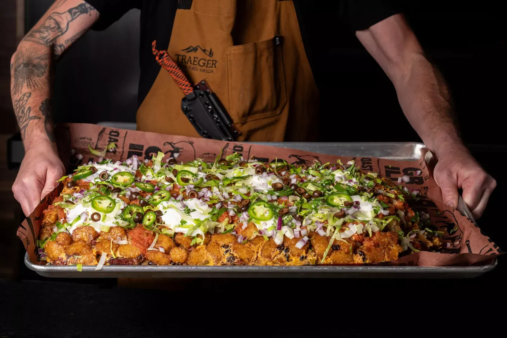 A man is holding a tray of food with a lot of toppings on it.