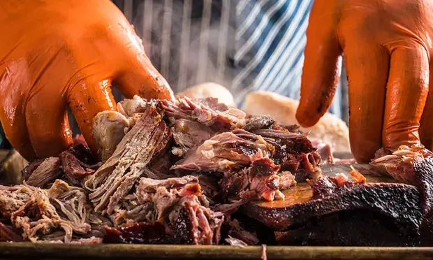 A person wearing orange gloves is cooking meat on a grill.