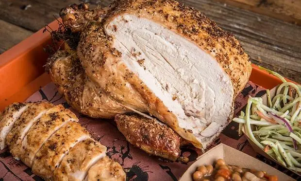 A close up of a roasted chicken on a tray with coleslaw and beans.