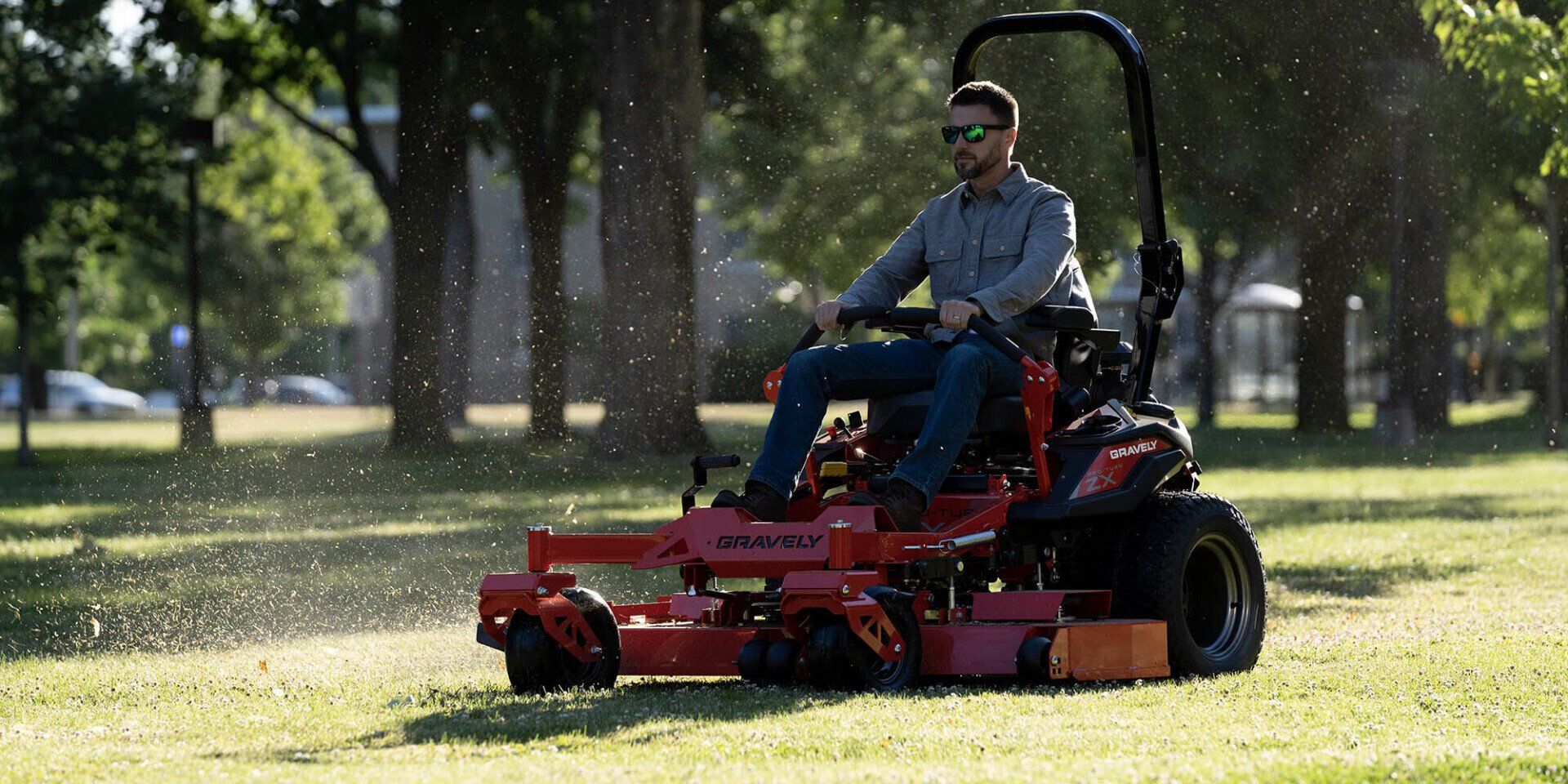 A man is riding a gravely  mower in a park.