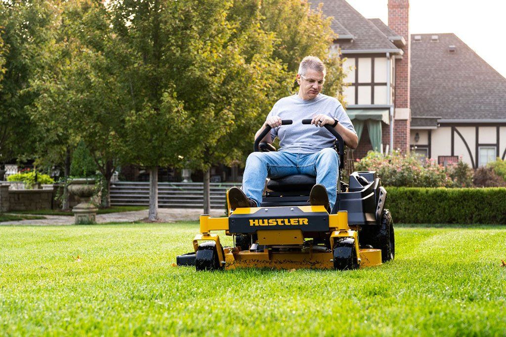 A man is riding a yellow lawn mower on a lush green lawn.