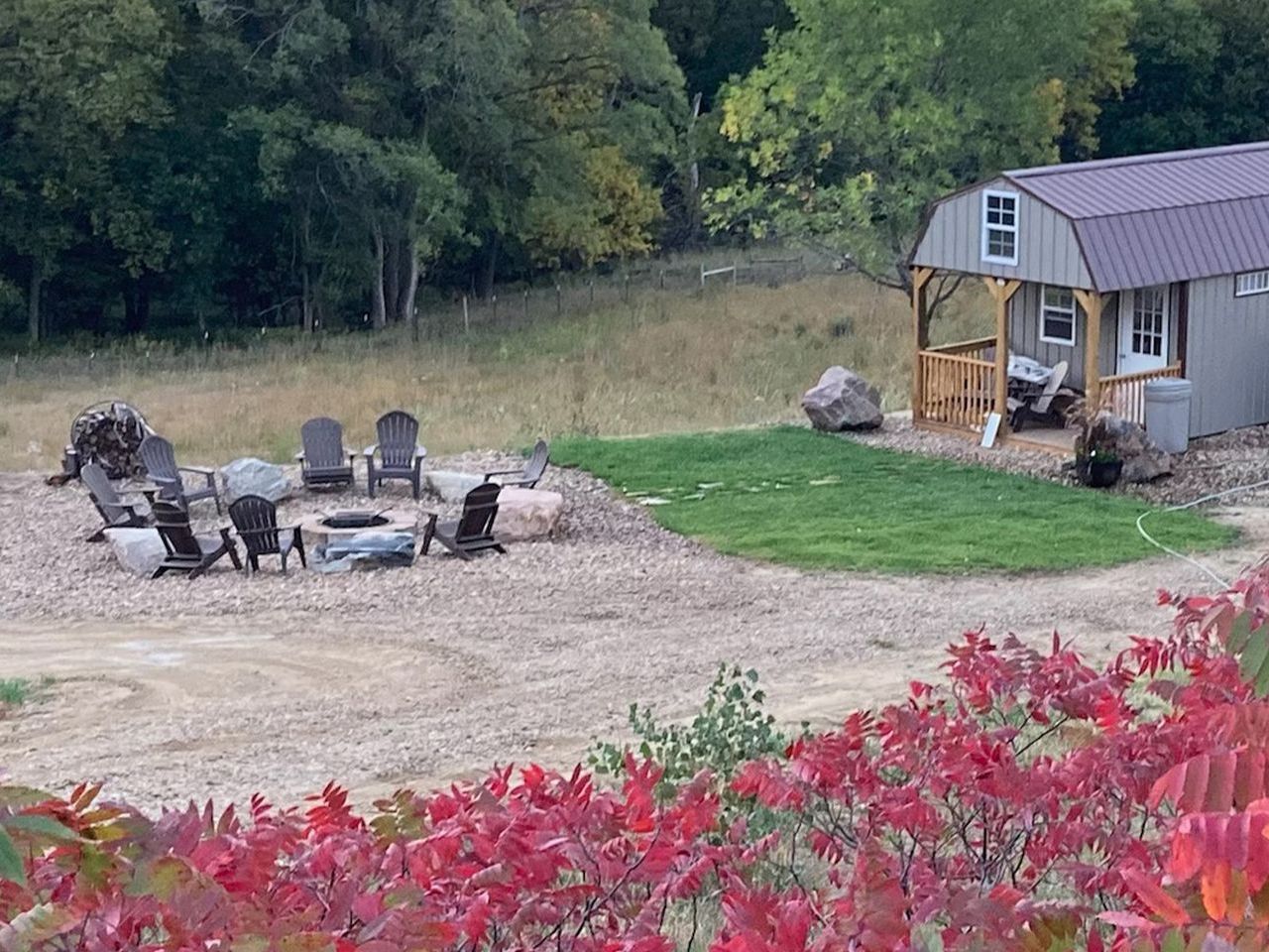 There is a fire pit in the middle of a field next to a barn.