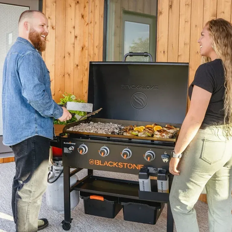 A man and a woman are cooking on a blackstone grill