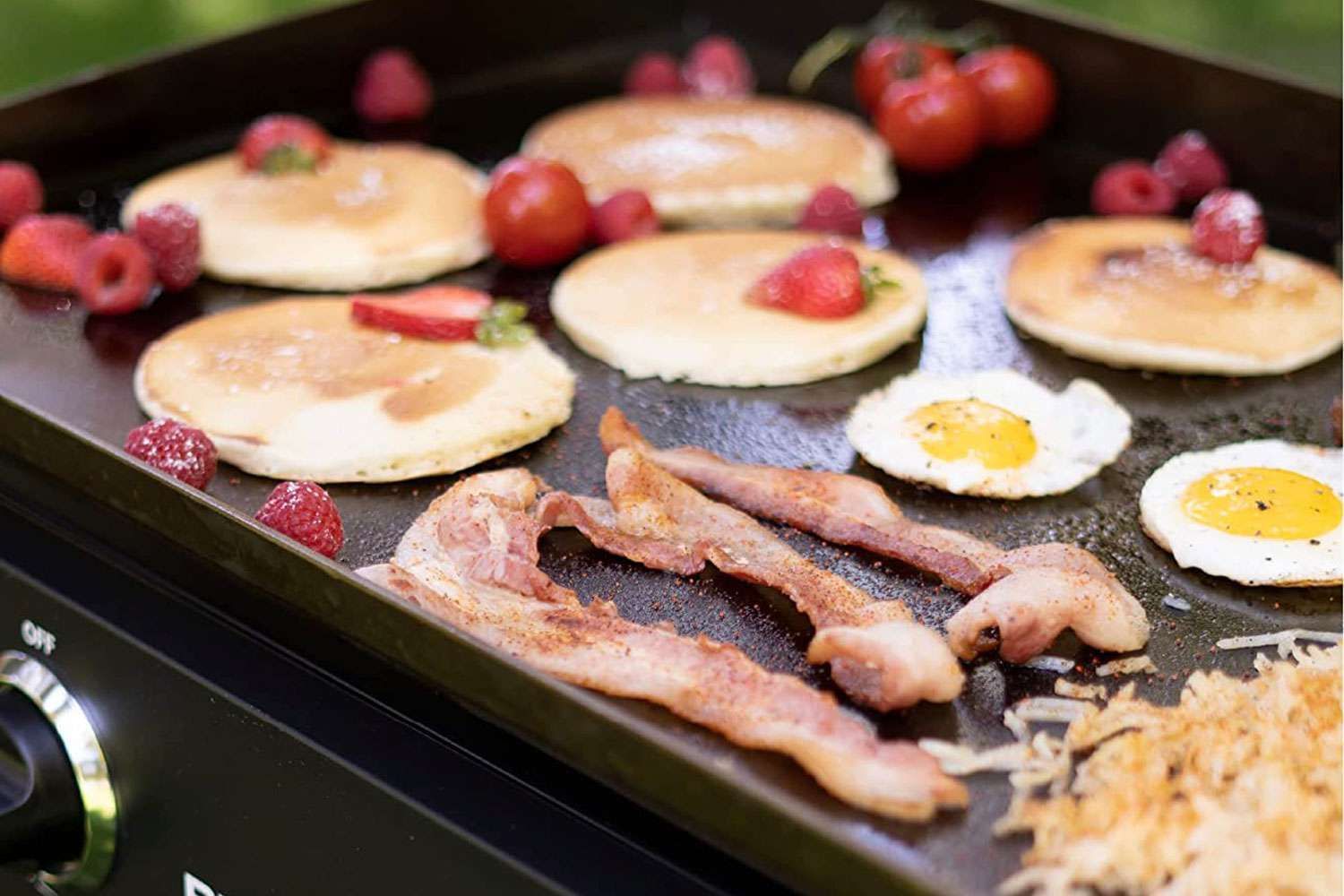 Pancakes , eggs , bacon and raspberries are being cooked on a Blackstone grill.