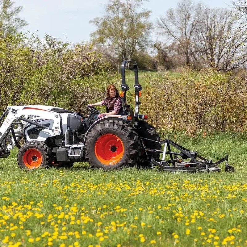 A woman is driving a Bobcat compact tractor through a field of dandelions.