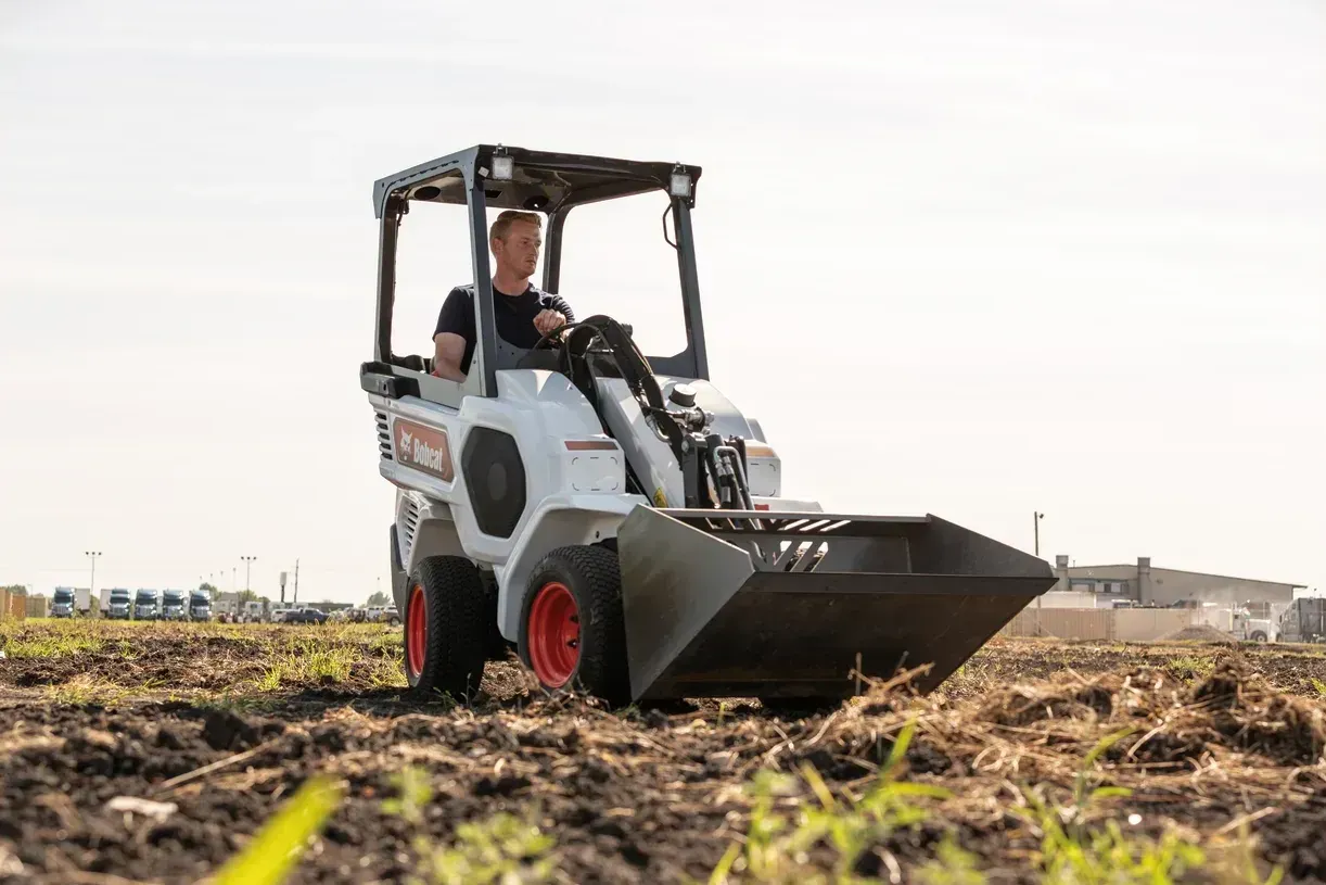 A man is driving a bobcat loader in a field.