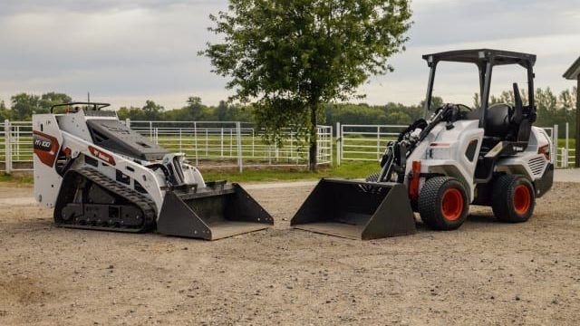 two bobcat tractors are parked next to each other in a dirt lot .