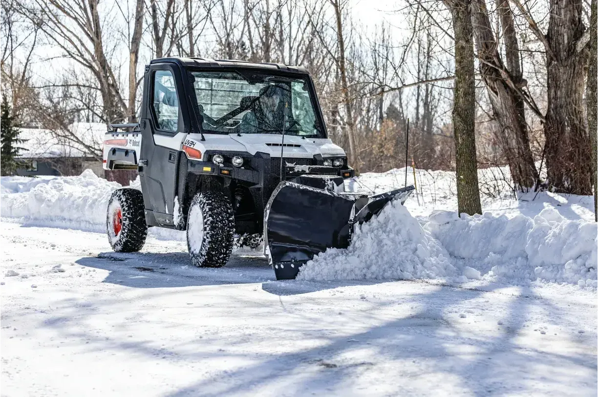 A utility vehicle is plowing snow on a snowy road.