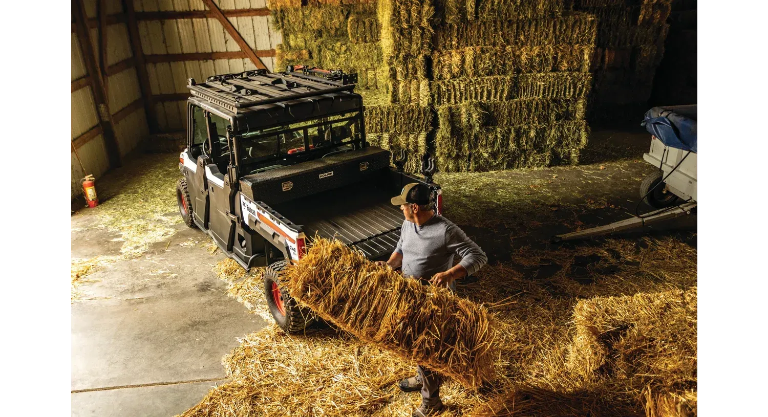 A man is carrying a large bale of hay in a barn.