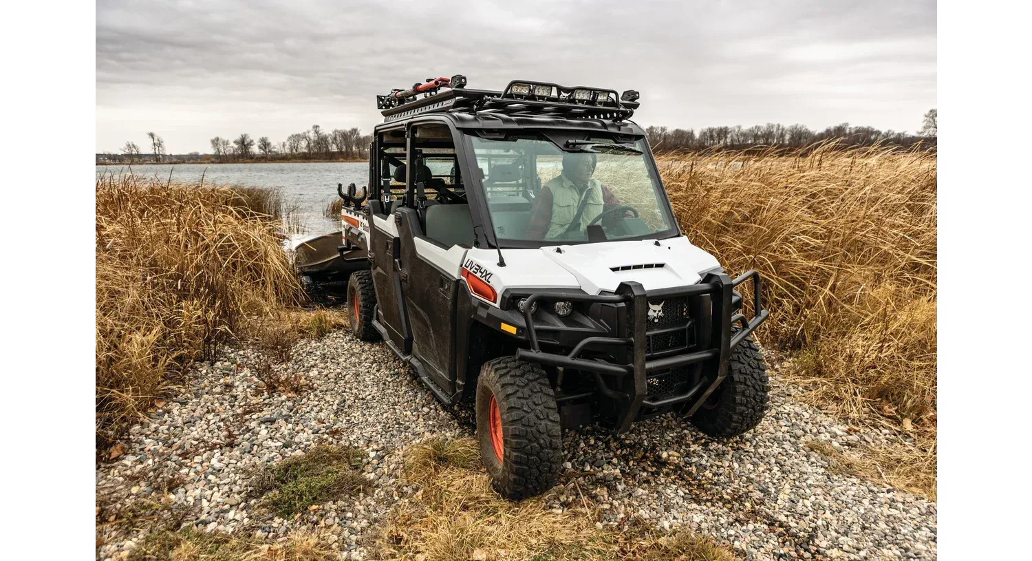 A white bobcat side by side is parked on a gravel road next to a body of water.