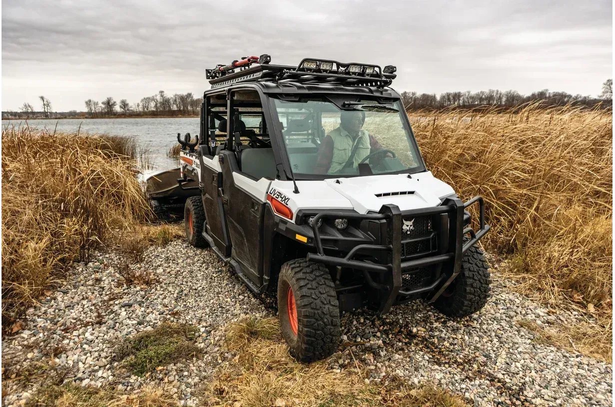 A white bobcat side by side is parked in a field next to a body of water.