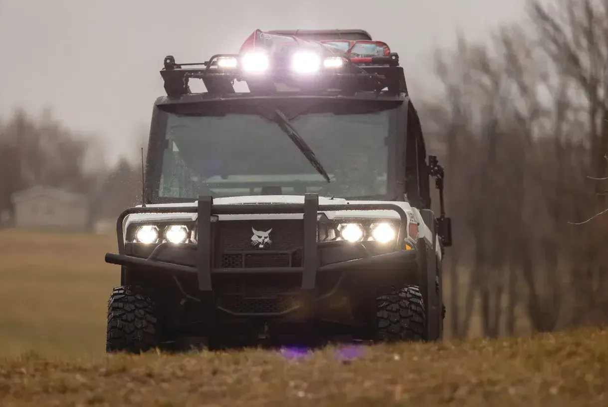 A bobcat side by side is driving down a dirt road in a field.