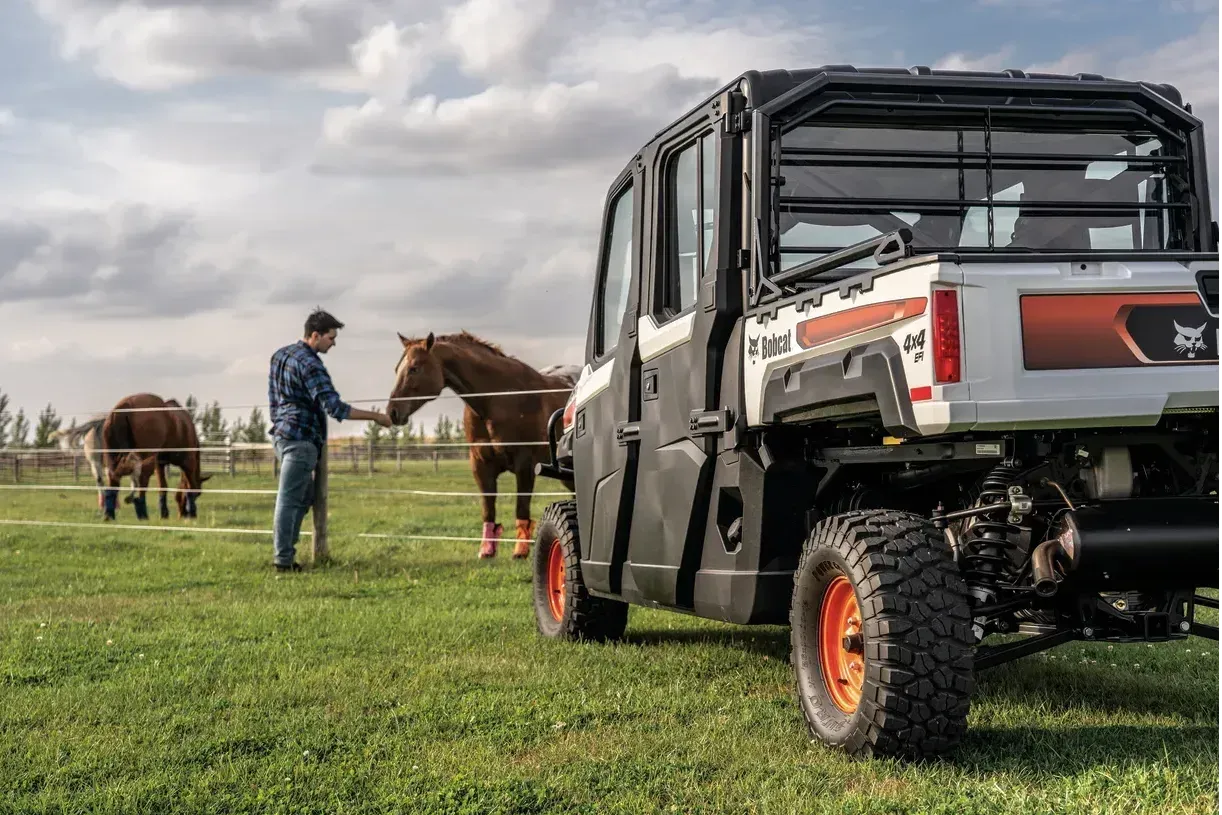 Un hombre está parado junto a un caballo en un campo junto a un vehículo.