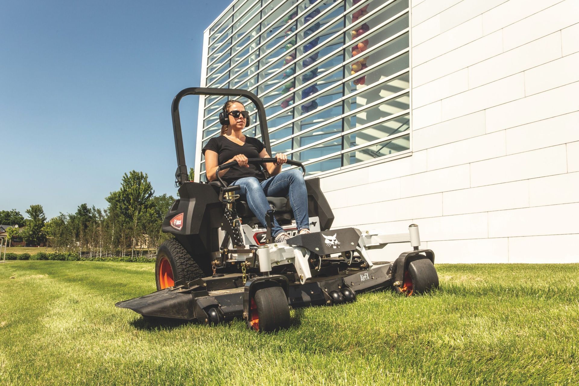 A woman is sitting on a lawn mower in front of a building.
