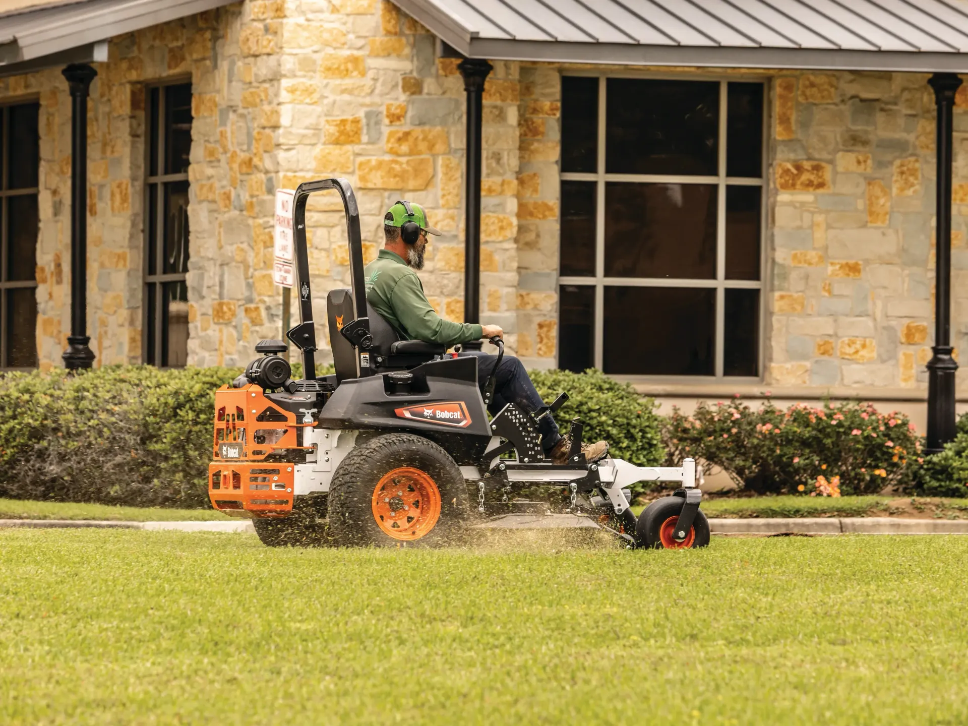 a man is riding a bobcat lawn mower in front of a stone building