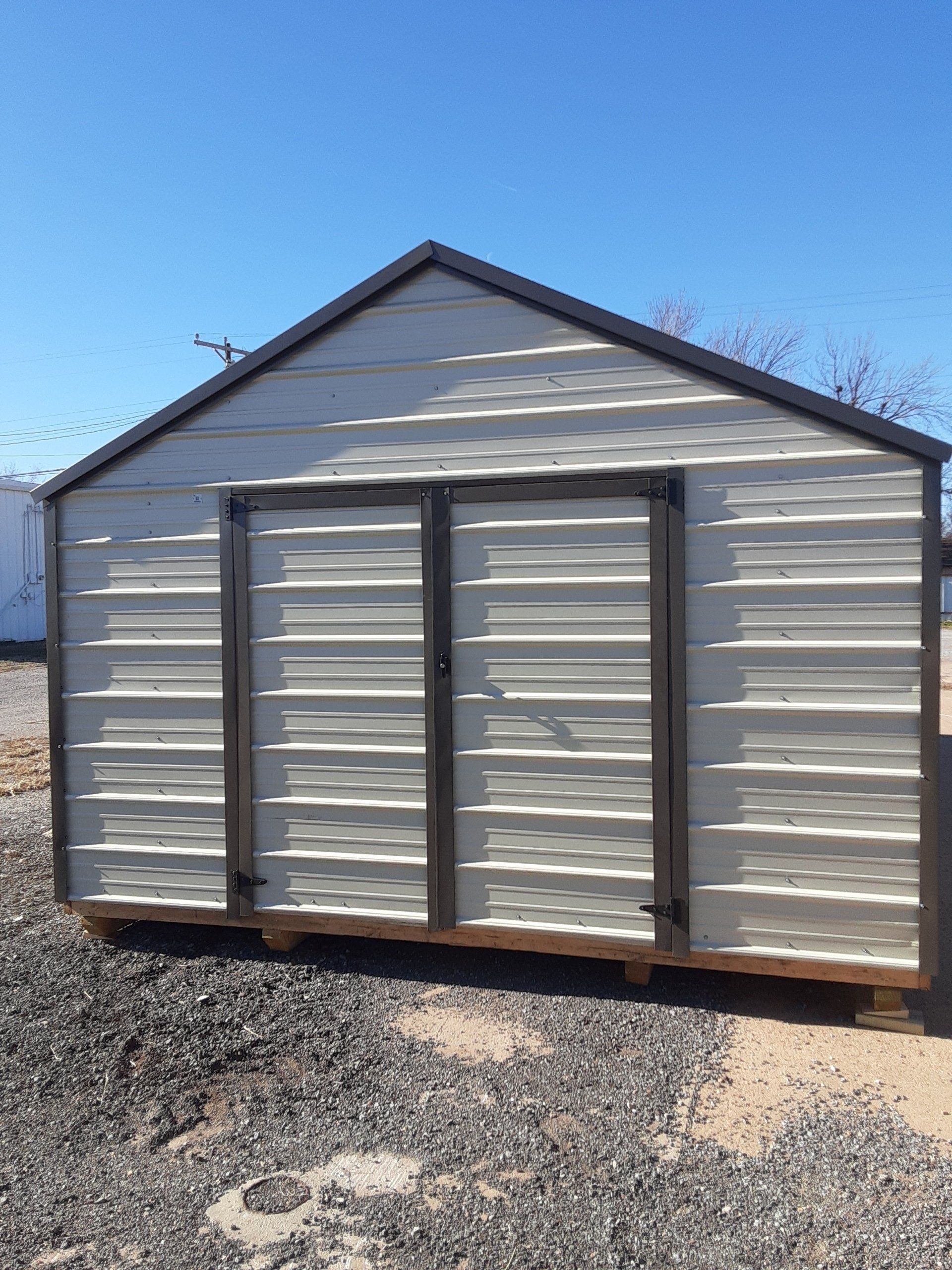 a metal portable shed with two doors is sitting on top of a gravel lot .