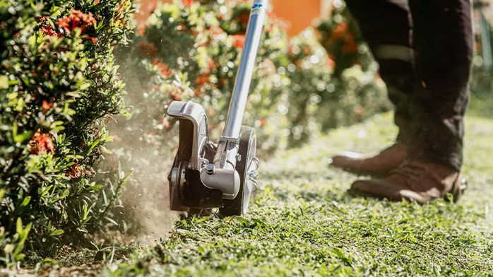 A lawn mower is cutting the grass on the sidewalk