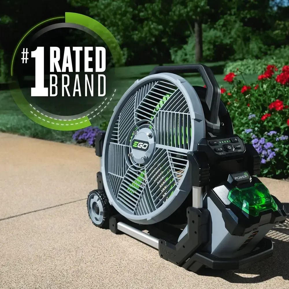 A portable fan is sitting on a sidewalk next to a garden.