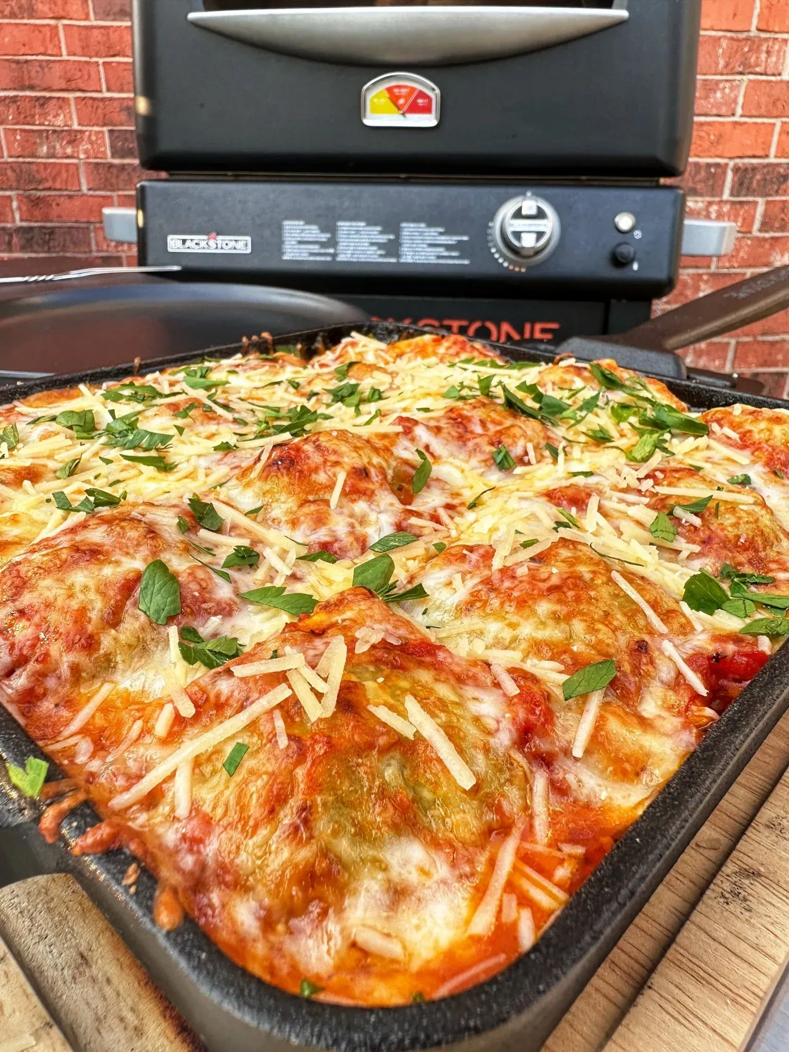 A pan of lasagna is sitting on a wooden table in front of a grill.