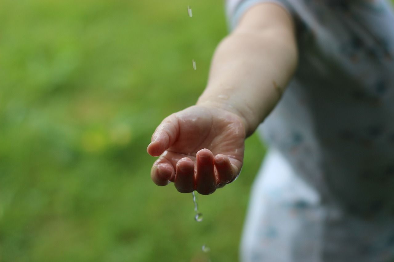 a child 's hand is reaching out to catch a drop of water