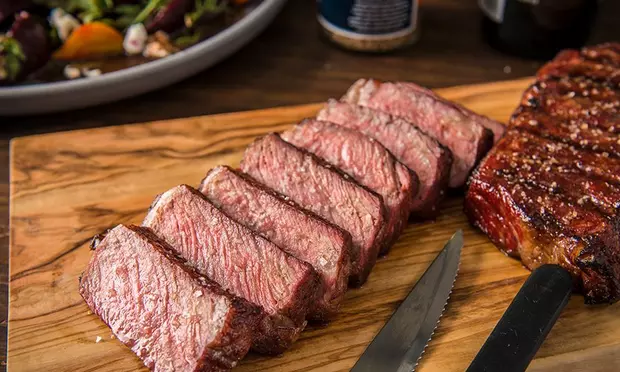 A steak on a wooden board with a knife next to it