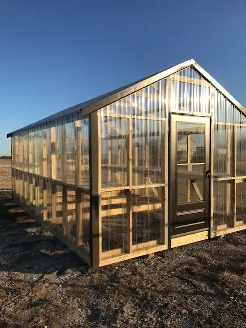 a greenhouse made of wood and clear plastic is sitting in the dirt .