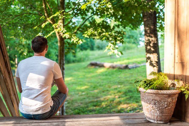 A man is sitting on a porch looking out a window.