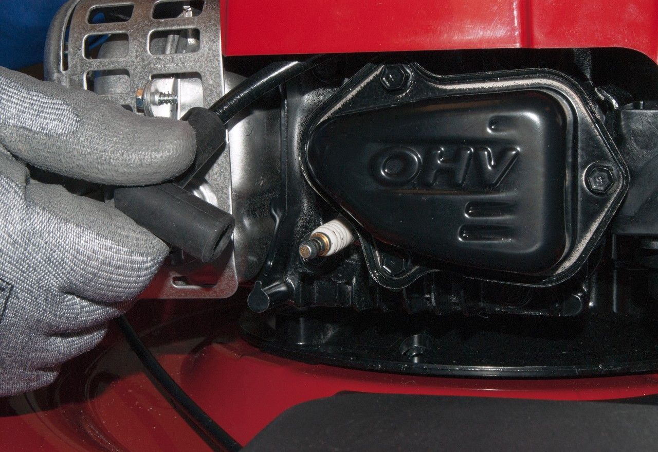 A person is fixing a lawn mower spark plug with a glove on.