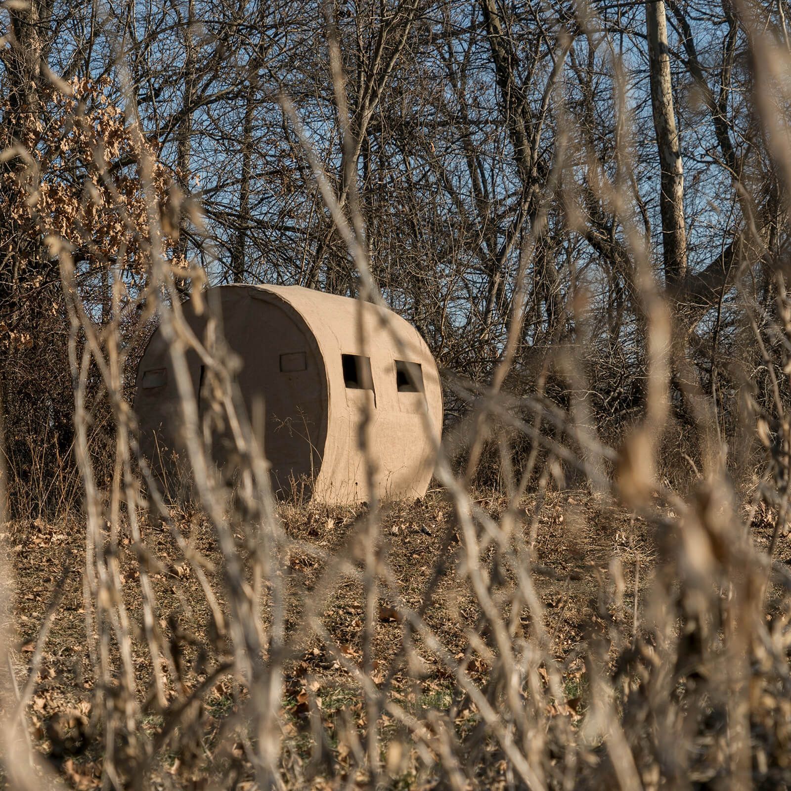 A tent is sitting in the middle of a field surrounded by trees.