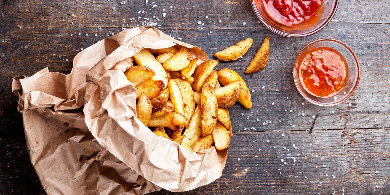 A bag of french fries and two bowls of ketchup on a wooden table.