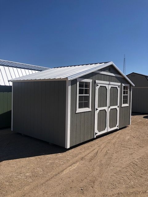A gray and white side utility shed with a white roof is sitting on top of a dirt field.