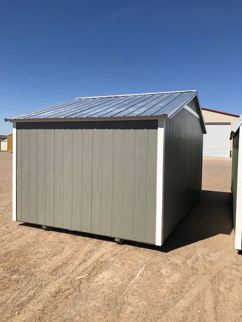 A small side utility shed with a metal roof is sitting in the middle of a dirt field.