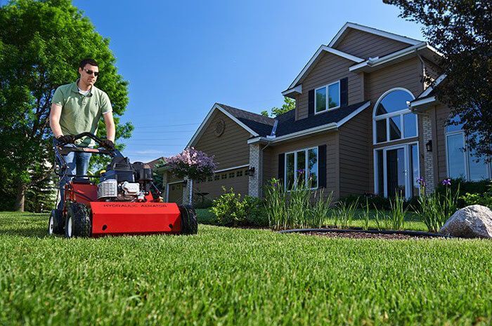 A man is mowing his lawn in front of a house.