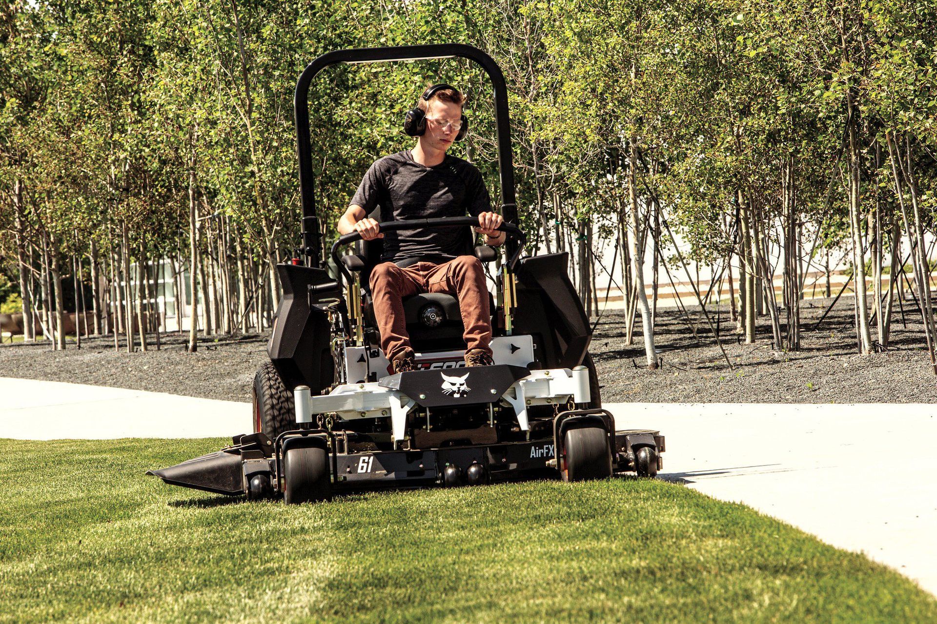 A man is riding a Bobcat ZT 6000 mower on a lush green lawn.