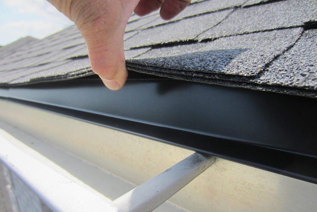 A picture of an inspector lifting up shingles to expose drip-edge metal on a roof.