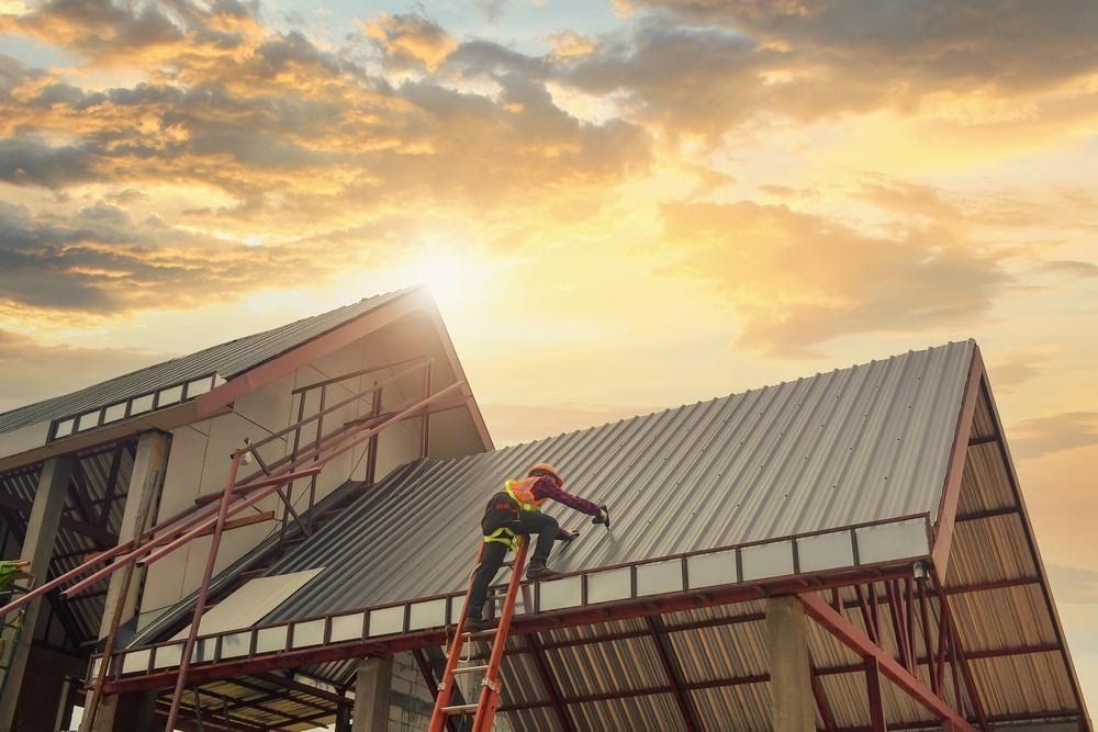 A worker standing on a ladder working on a standing-seam metal roof